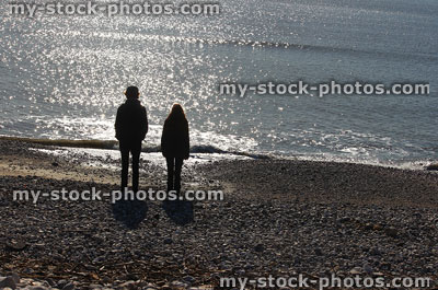 Stock image of silhouettes of children on pebble beach against sea