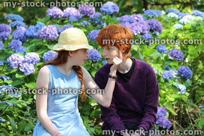 Stock image of boy and girl sitting on garden bench, face to face