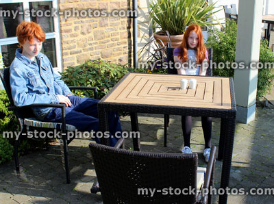 Stock image of teenage boy and young girl sitting outside at patio table