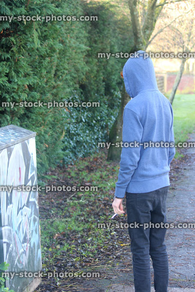 Stock image of teenage boy smoking underage / youth wearing hoodie / hood, graffiti, pathway