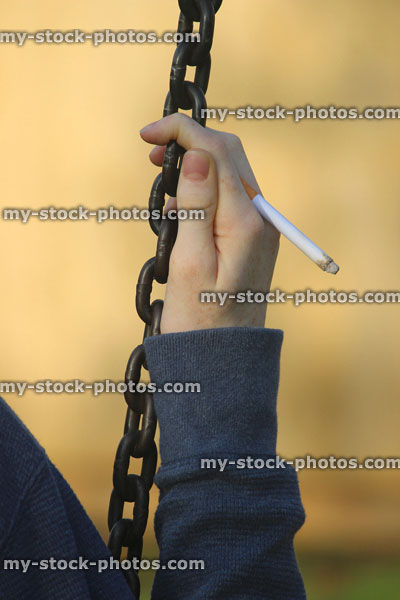 Stock image of teenage boy smoking underage / youth hand close up / hood, playground swing