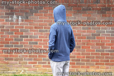 Stock image of teenage boy / youth wearing hoodie, beside dirty brick wall