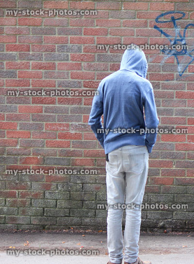 Stock image of teenage boy / youth wearing hoodie, beside graffiti brick wall