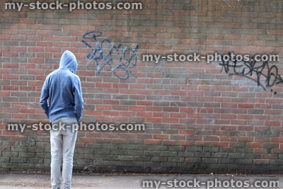 Photo of a teenage boy wearing a hoodie by a graffiti wall.