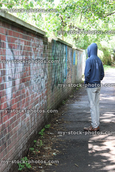 Stock image of teenage boy / youth wearing hoodie, beside graffiti wall