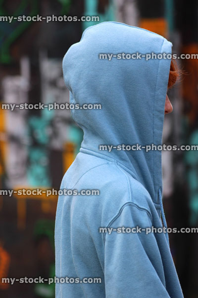 Stock image of teenage boy / youth wearing hoodie, beside graffiti wall
