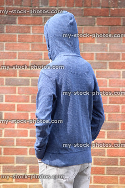 Stock image of teenage boy / youth wearing hoodie, beside graffiti brick wall