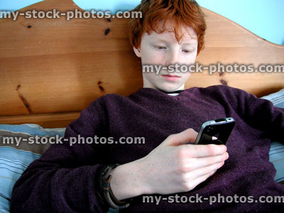 Stock image of teenage boy using a smartphone on his bed