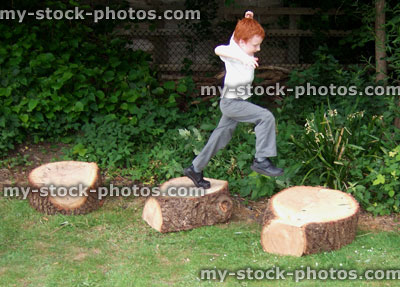 Stock image of young boy in school playground, jumping on logs