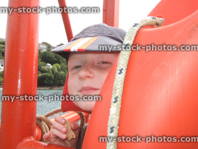 Stock image of freckled boy looking through lifering at seaside, wearing cap