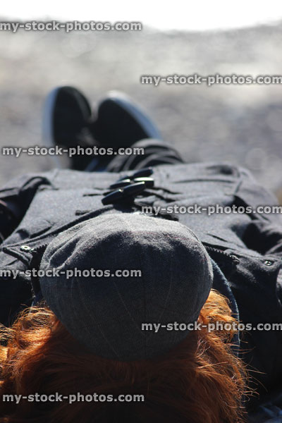 Stock image of teenage boy lying on winter beach, wearing duffle coat cap