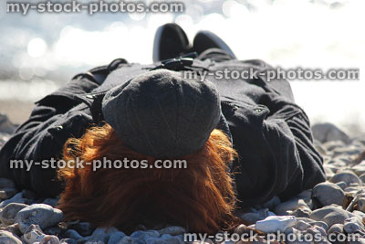 Stock image of teenage boy sunbathing in winter on pebble beach