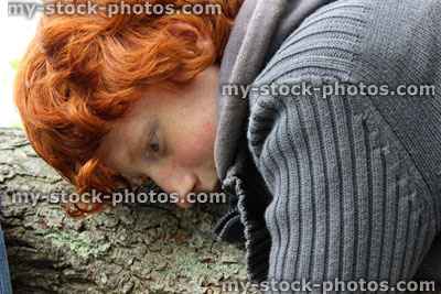 Stock image of boy with red hair lying against tree branch