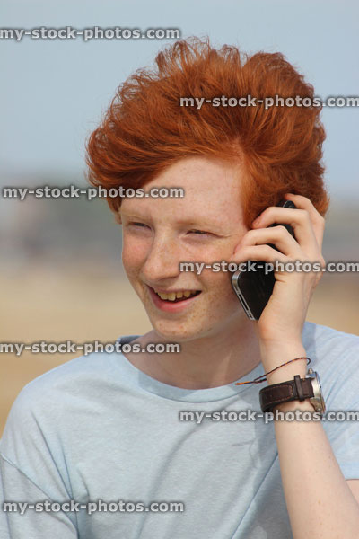 Stock image of teenage boy using mobile phone, speaking, laughing, beach