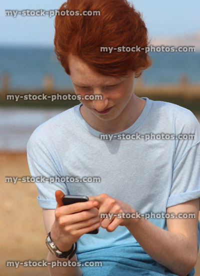 Stock image of boy texting on his mobile phone, seaside beach