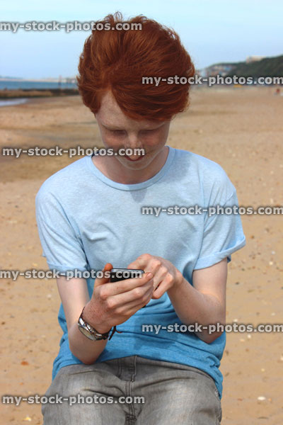 Stock image of boy texting on his mobile phone, seaside beach