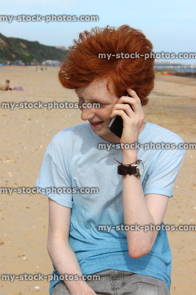Stock image of teenage boy using mobile phone, speaking, laughing, beach