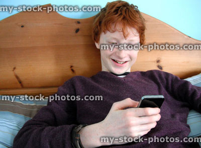 Stock image of teenage boy using a smartphone on his bed