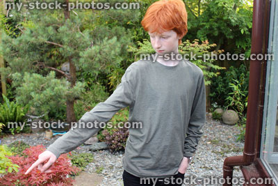 Stock image of young teenage boy pointing with finger in garden