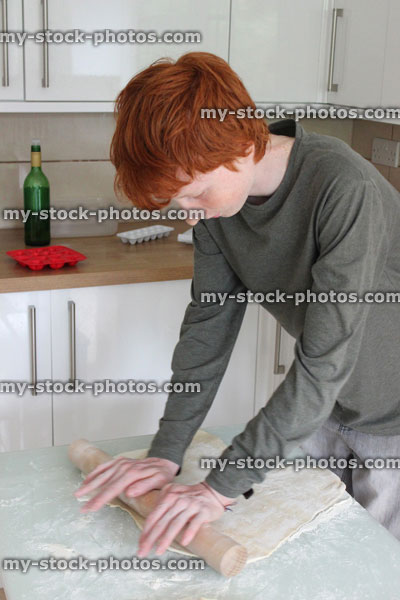 Stock image of teenage boy rolling pastry in kitchen, baking / cooking