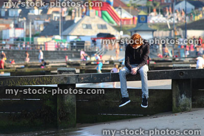 Stock image of red hair teenage boy sitting on wooden groyne at seaside beach