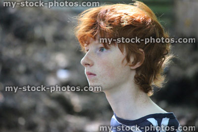 Stock image of teenage boy sitting in woodland garden, daydreaming, looking into distance