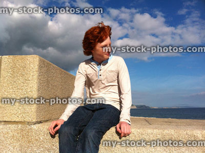 Stock image of red headed boy sat on seawall in sunshine