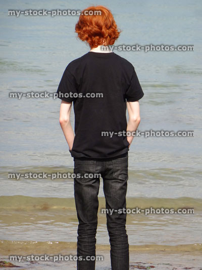 Stock image of boy standing on sandy beach looking towards sea