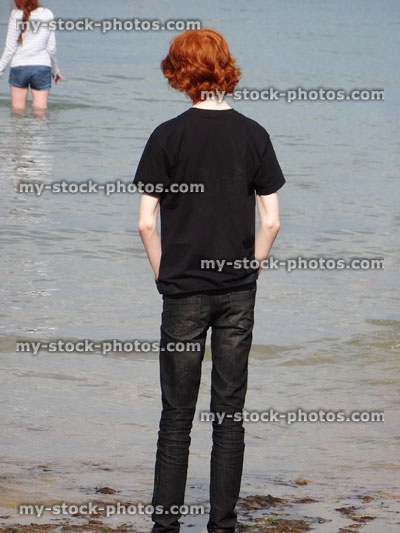 Stock image of tall boy from behind, standing on beach next-to-sea