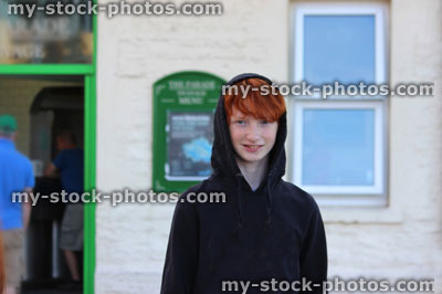 Stock image of young teenage boy, black hoodie / red hair, standing outside pub / public house