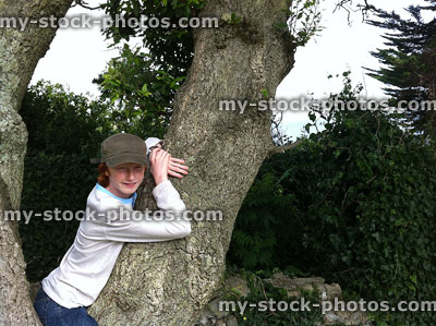 Stock image of boy leaning against rough tree trunk, wearing cap