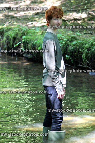 Stock image of boy wading / paddling, shallow river with green wellies / wellington boots