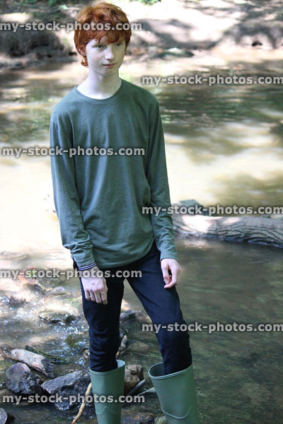 Stock image of boy wading / paddling, shallow river with green wellies / wellington boots
