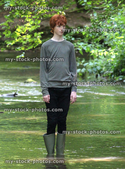 Stock image of boy wading in shallow river with green wellies / wellington boots