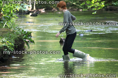 Stock image of boy wading in shallow river with green wellies / wellington boots