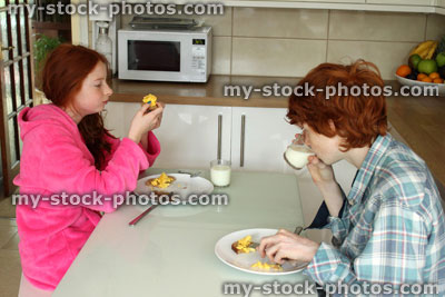Stock image of children (boy and girl) eating healthy breakfast at kitchen table