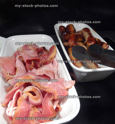 Stock image of full English fried breakfast buffet, bacon, sausages, serving tongs