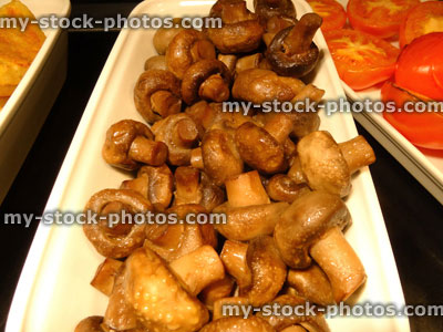Stock image of full English fried breakfast buffet, fried mushrooms, grilled tomatoes, serving tongs