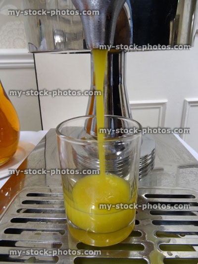 Stock image of orange juice dispenser, tap pouring breakfast fresh fruit juice into glass