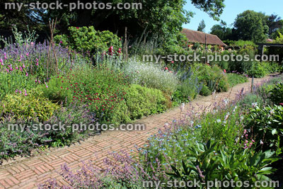 Stock image of red brick path through herbaceous flower border, cottage garden