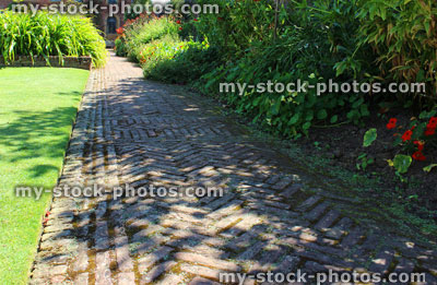 Stock image of red brick path, block paving, paved pathway, herringbone pattern, lawn, shady garden