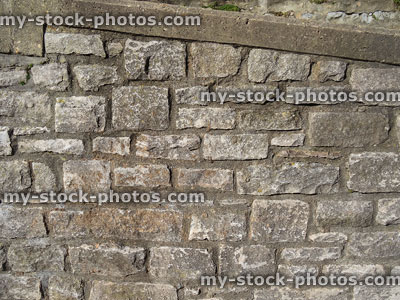 Stock image of sloping weathered grey stone / limestone block wall, cement mortar
