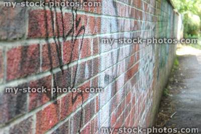 Stock image of dirty brick wall, wall covered in graffiti, rundown, overgrown alleyway