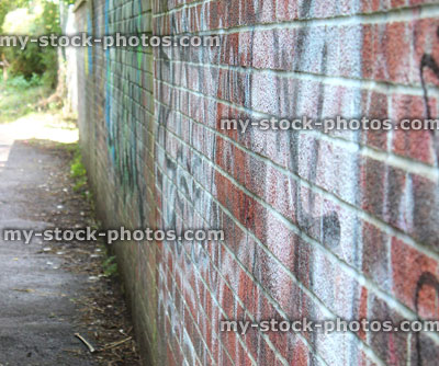 Stock image of dirty brick wall, wall covered in graffiti, rundown, overgrown alleyway