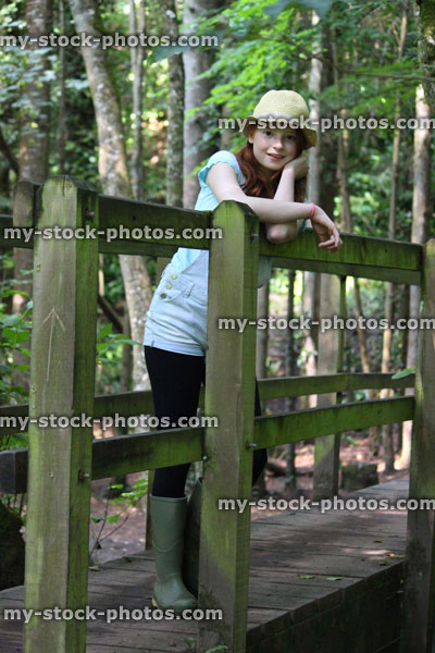 Stock image of girl in woodland, standing on wooden bridge railings