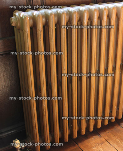 Stock image of old fashioned cast iron radiator on wooden floor, painted brown