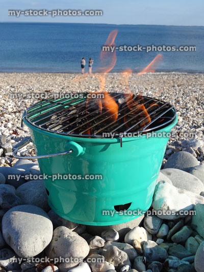Stock image of portable bucket barbecue on beach with charcoal flames