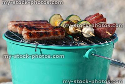 Stock image of chipolata sausages on charcoal barbecue bucket painted green