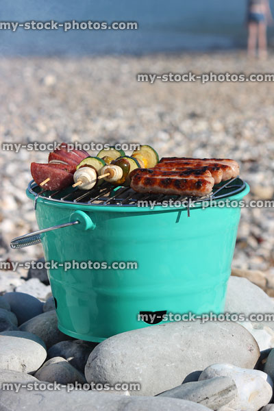 Stock image of barbecue in metal bucket cooking sausages by the sea