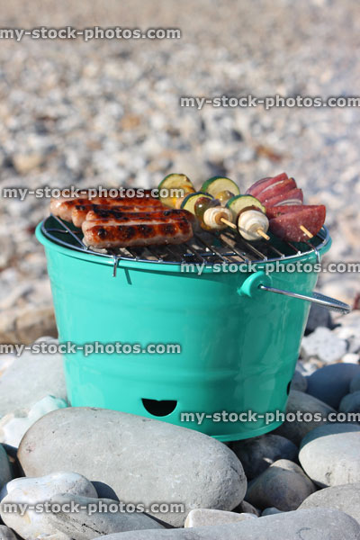 Stock image of painted bucket bbq with sausages and kebabs, on large pebbles